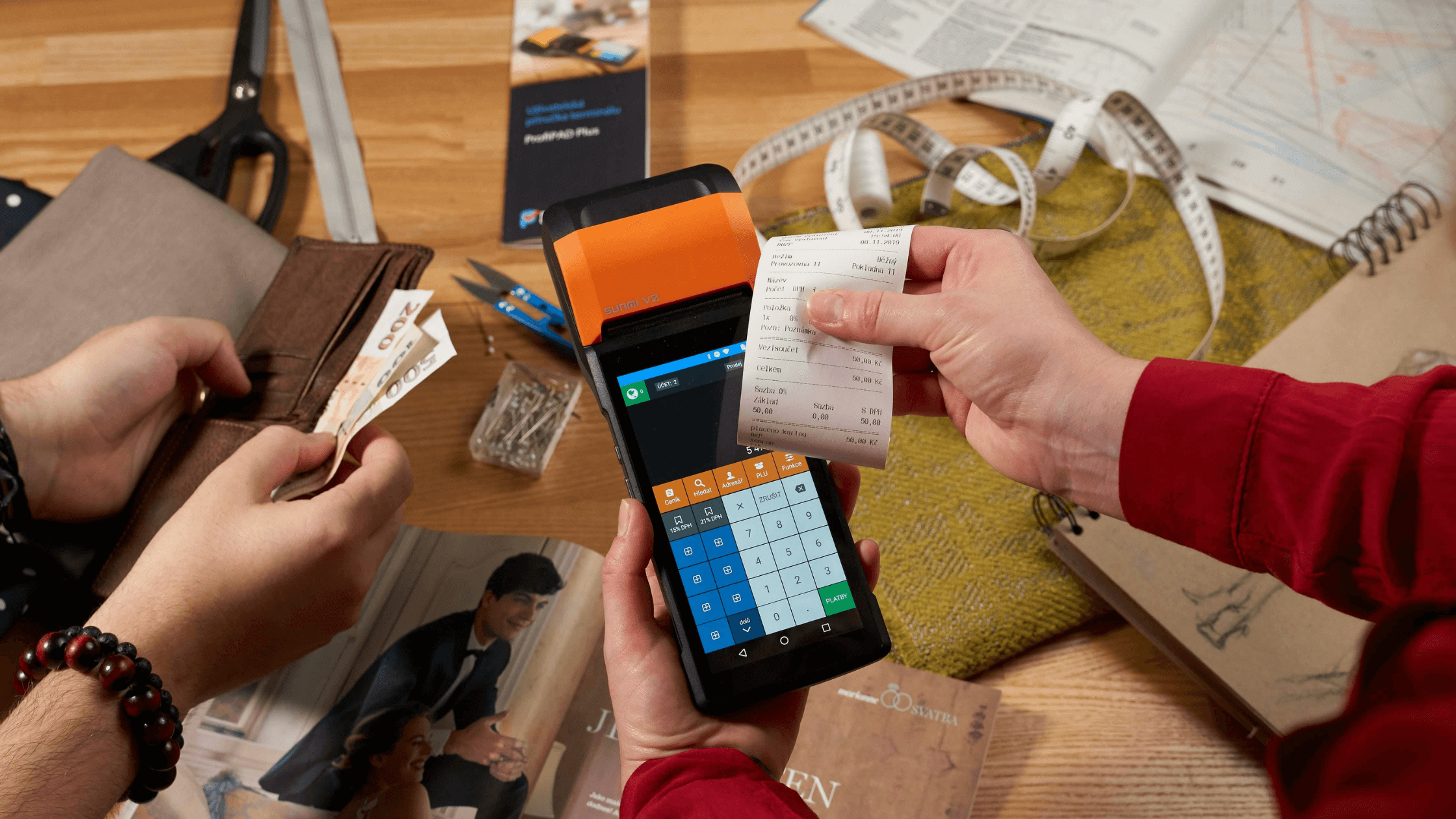 Close-up of a mobile POS device printing a receipt while a customer pays with cash.