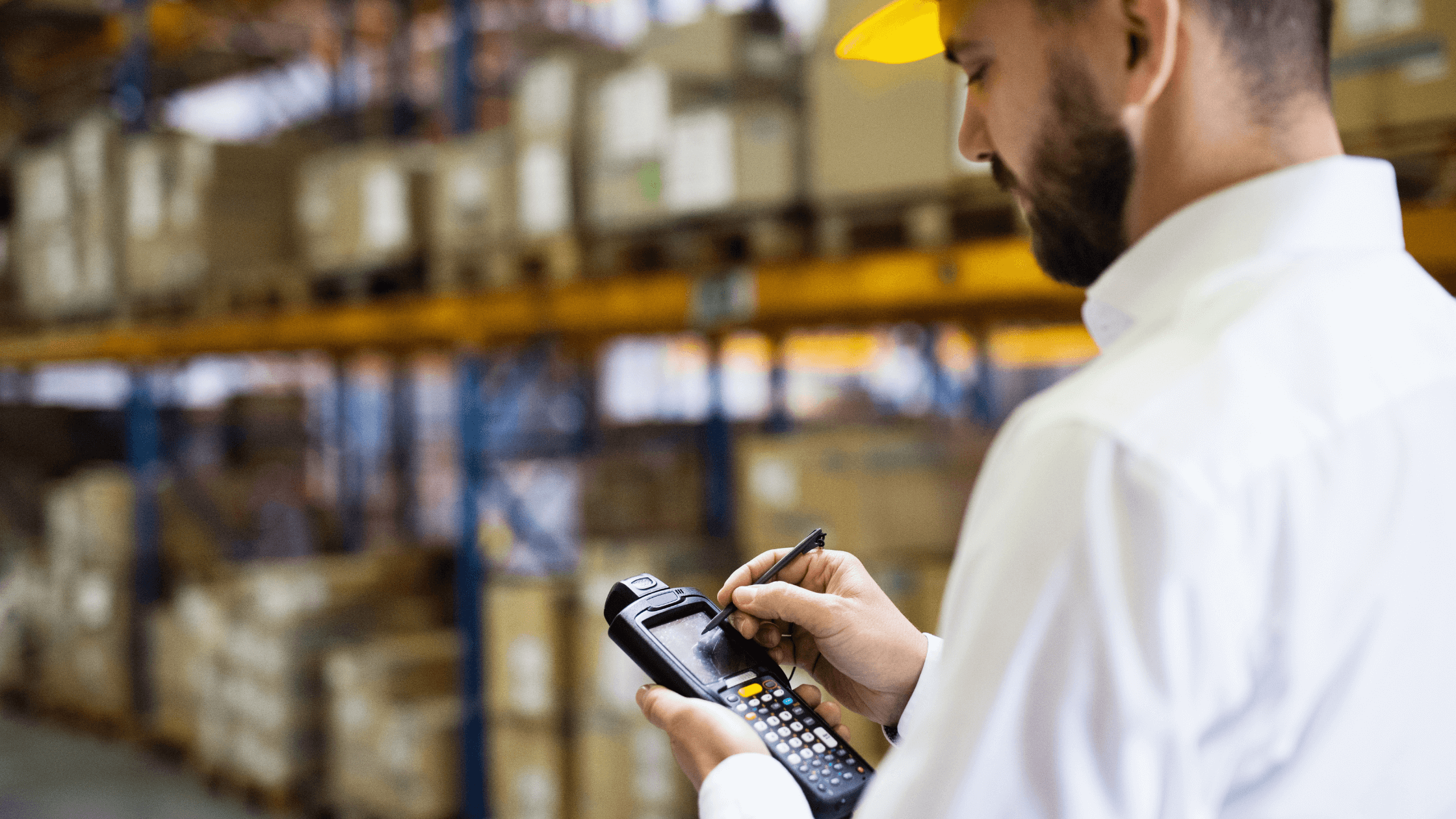 Worker using a handheld barcode scanner and tablet device in a warehouse to manage stock and inventory tracking.
