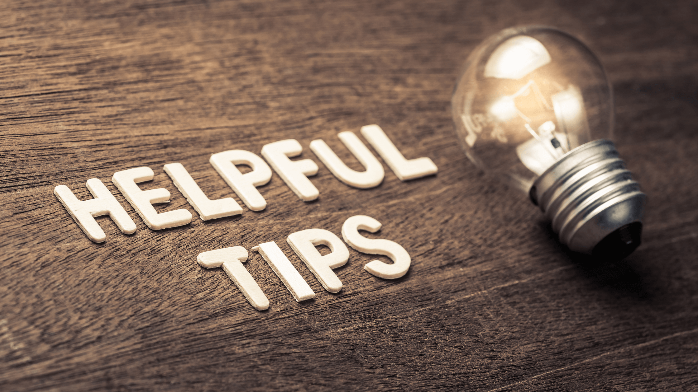 Wooden table with the words 'HELPFUL TIPS' written beside a glowing light bulb, symbolizing guidance and useful advice.