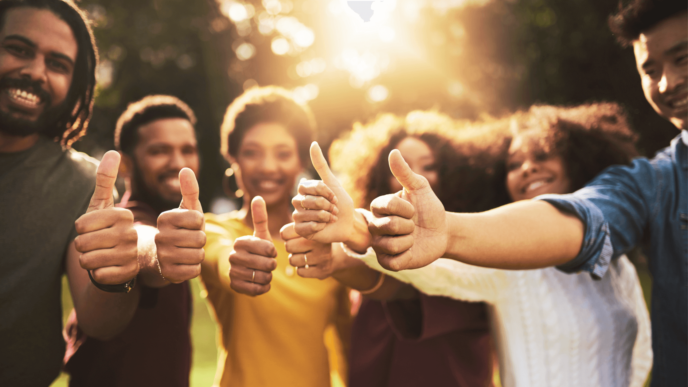 Group of people smiling and showing thumbs up in sunlight.