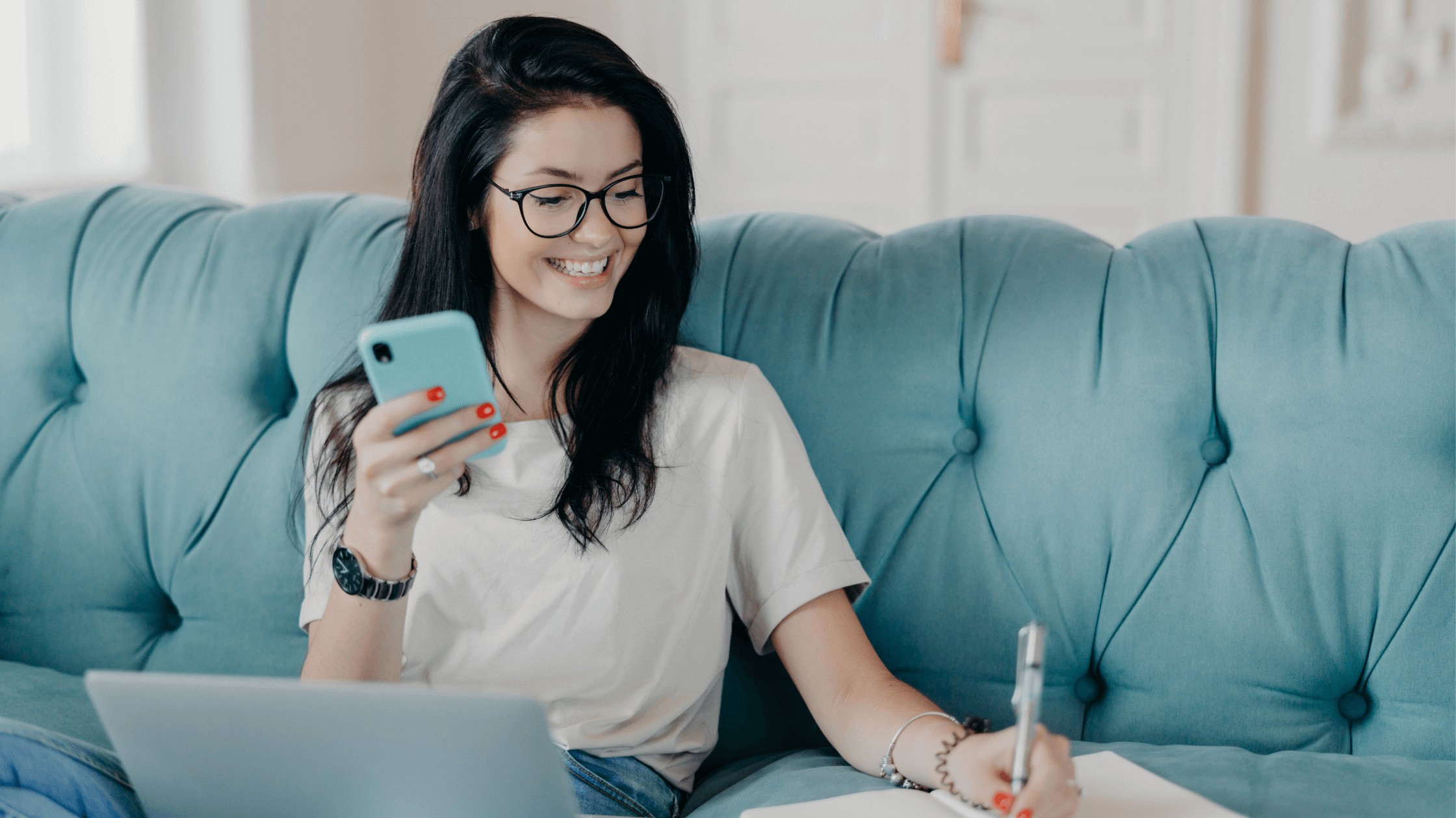 Smiling woman using smartphone and laptop while working from home.